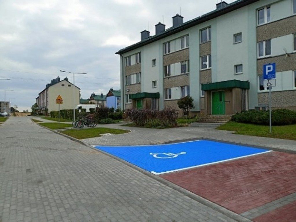 Niebieskie miejsce parkingowe dla osób z niepełnosprawnościami przed blokiem mieszkalnym