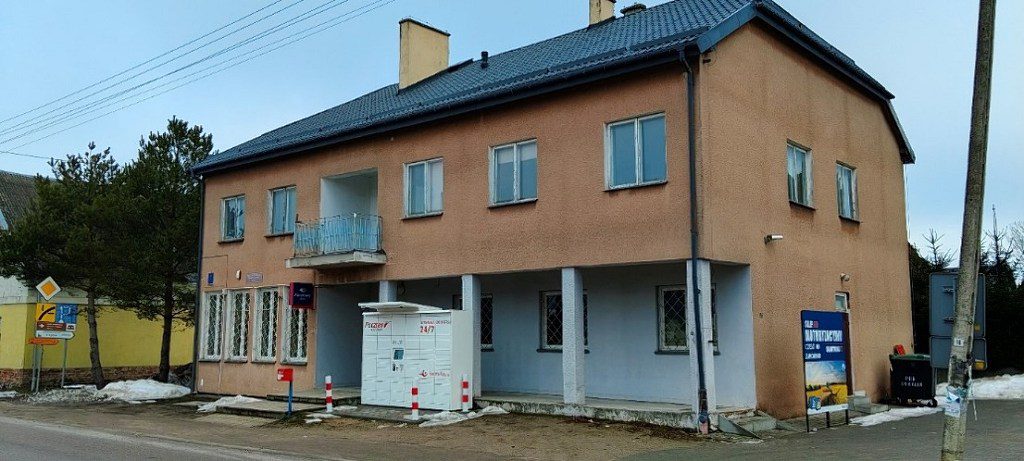 Piętrowy, brzoskwiniowy budynek z automatem paczkowym Pocztex 24/7 przed wejściem