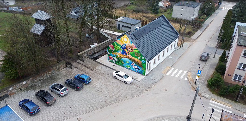 Widok z góry na budynek z kolorowym muralem przedstawiającym dziecko, słońce i zwierzęta