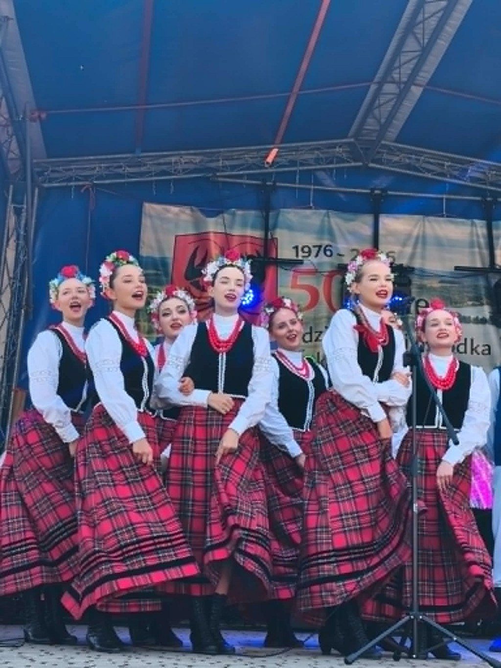 Grupa dziewcząt w tradycyjnych strojach ludowych śpiewa na scenie podczas występu