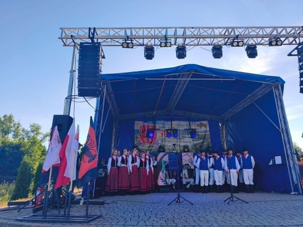 Zespół ludowy w tradycyjnych strojach występuje na zadaszonej scenie plenerowej