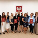 Grupa osób z teczkami Gminy Filipów pozuje do pamiątkowego zdjęcia na tle godła Polski