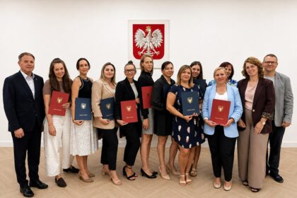 Grupa osób z teczkami Gminy Filipów pozuje do pamiątkowego zdjęcia na tle godła Polski