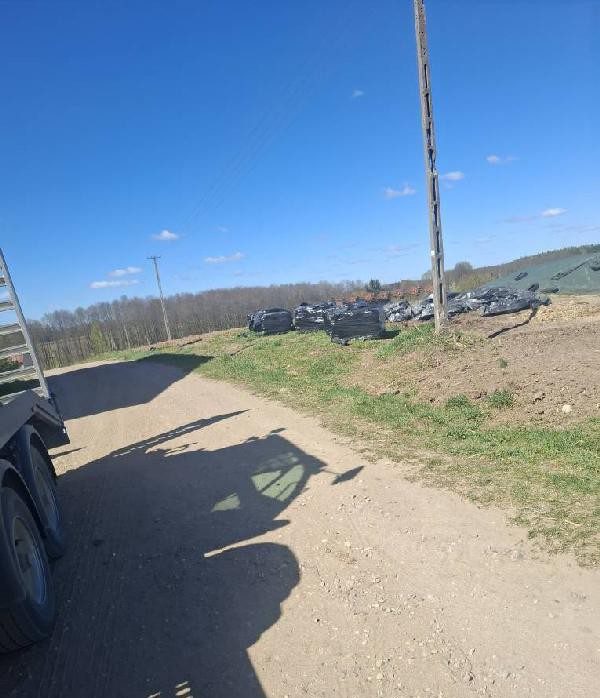 Palety z azbestem owinięte czarną folią leżące na wzniesieniu przy gruntowej drodze