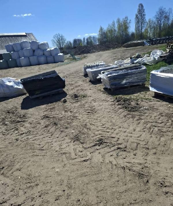 Palety z azbestem owiniętymi folią na piaszczystym placu obok stosu bel siana
