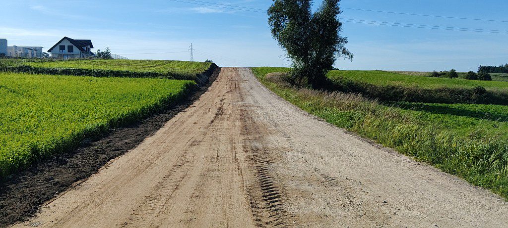 Szeroka droga gruntowa prowadząca pod górę wśród zielonych pól
