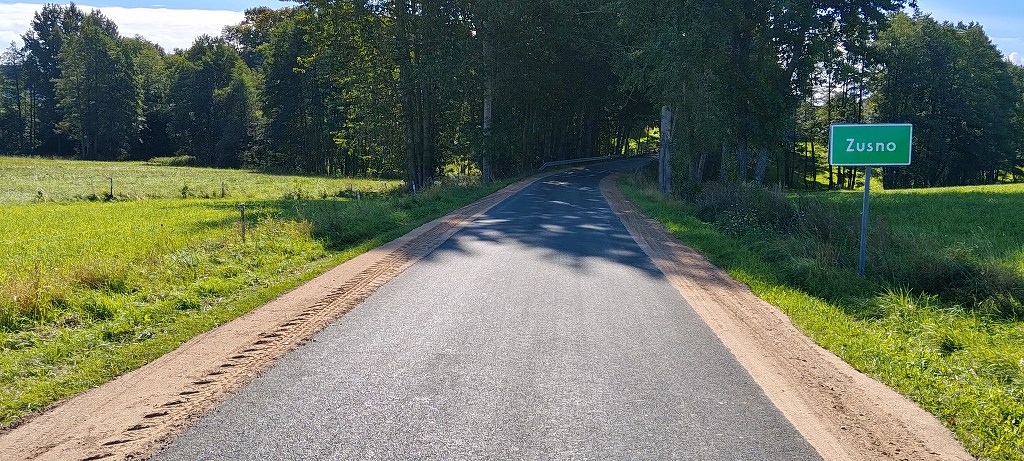 Asfaltowa droga prowadząca do miejscowości Zusno z zieloną tablicą wjazdową