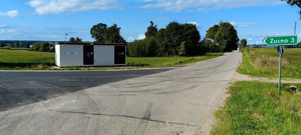 Asfaltowa droga wiejska ze stacją transformatorową po lewej i drogowskazem z napisem Zusno 3 po prawej
