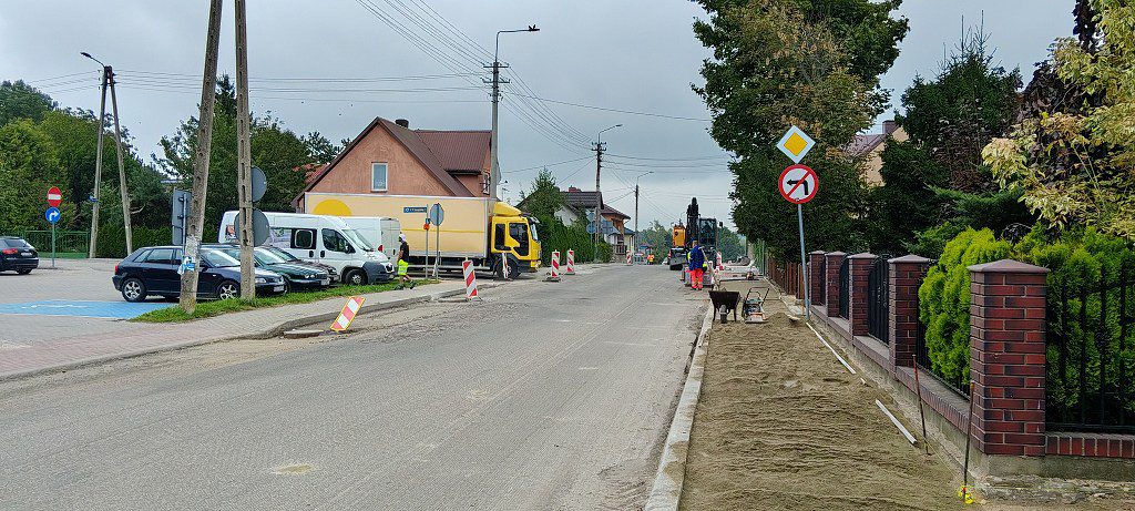 Remont chodnika i jezdni na osiedlowej ulicy z widocznym sprzętem budowlanym oraz drogowcami