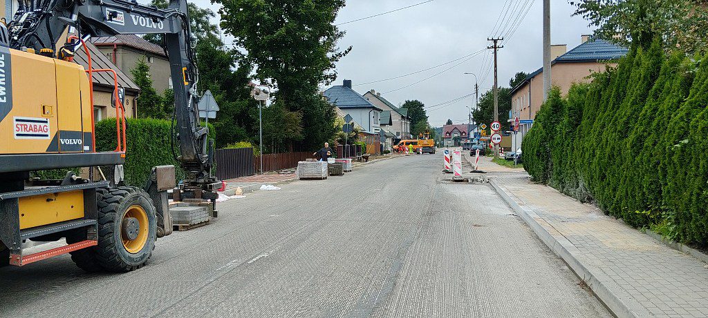 Żółta koparka Volvo i palety z kostką brukową na remontowanej ulicy w terenie zabudowanym