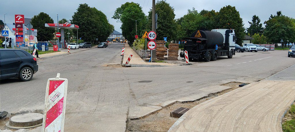 Remont ulicy ze słupkami ostrzegawczymi, ciężarówką drogową i stacją paliw w tle