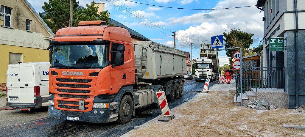 Pomarańczowa ciężarówka Scania stojąca na remontowanym odcinku drogi podczas prac drogowych