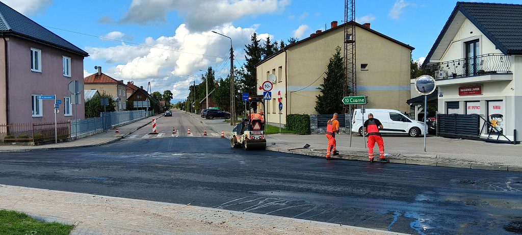 Drogowcy pracujący przy układaniu nowej nawierzchni asfaltowej na skrzyżowaniu ulic z użyciem walca