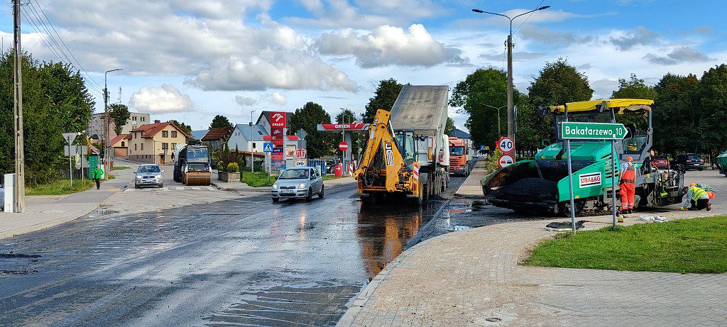 Prace drogowe i maszyny układające nowy asfalt na ulicy z drogowskazem Bakałarzewo