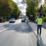 Mężczyźni w żółtych kamizelkach odblaskowych stojący na chodniku przy ulicy obok stacji paliw