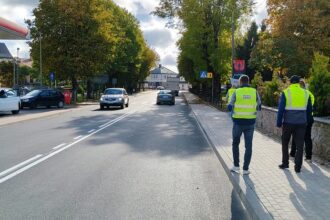 Mężczyźni w żółtych kamizelkach odblaskowych stojący na chodniku przy ulicy obok stacji paliw