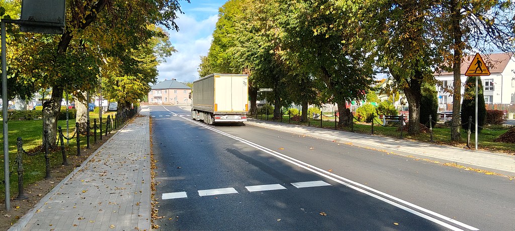 Ciężarówka jadąca asfaltową drogą otoczoną drzewami i chodnikiem