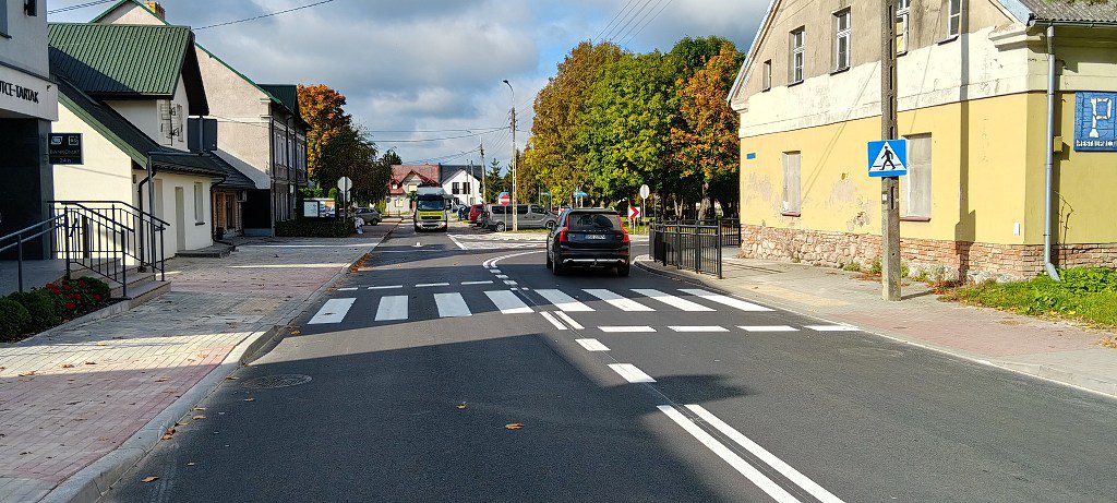 Ulica w miasteczku z przejściem dla pieszych, jadącym samochodem i budynkami po obu stronach