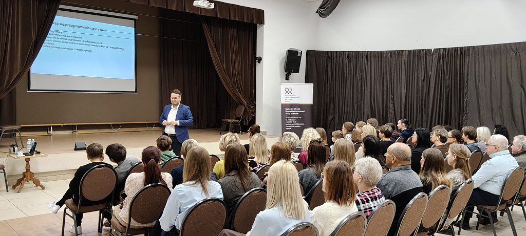 Prelegent prowadzi wykład na scenie przed publicznością w sali wykładowej