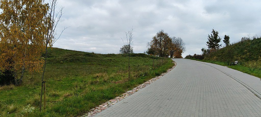 Wyłożona kostką alejka prowadząca pod górę wśród zielonych pagórków i jesiennych drzew