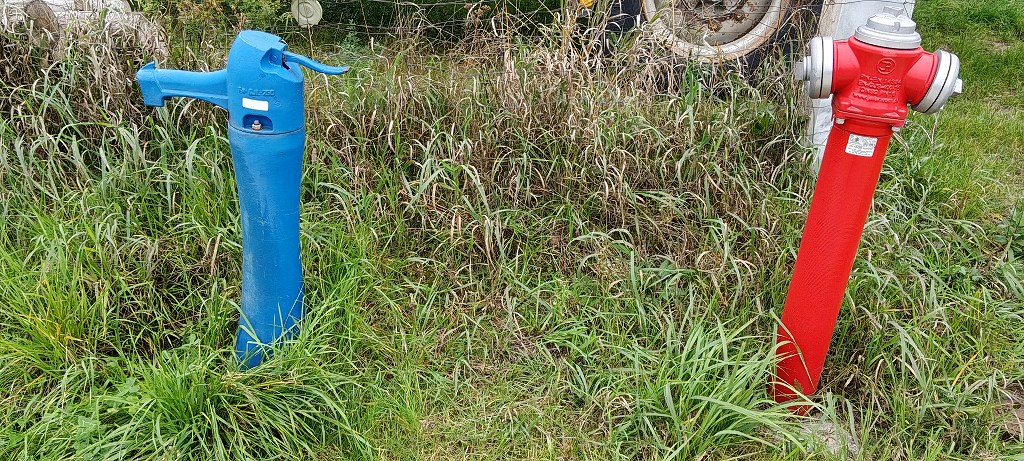 Niebieska ręczna pompa wodna i czerwony hydrant pożarowy stojące obok siebie w trawie